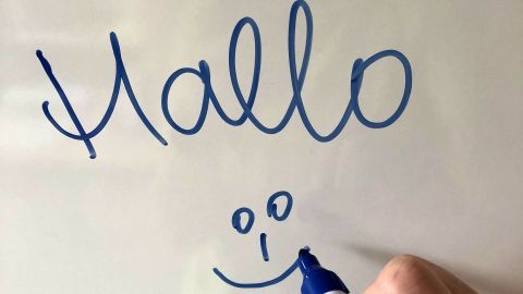 Ein Marker schreibt „Hallo“ und ein lächelndes Gesicht auf ein strahlend weißes Board in einem hellen Raum.