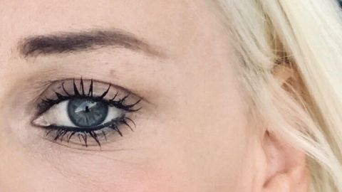 Betonte Augen durch aufwendige Mascara und auffälligen Schmuck in einer hellen Umgebung. Die Person trägt auffällige Ohrringe.