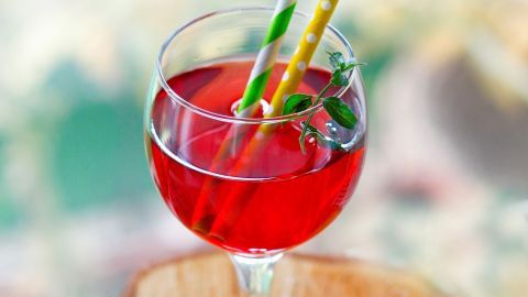 Ein Glas mit rotem Getränk steht auf einem Holzuntergrund, verziert mit zwei bunten Strohhalmen.