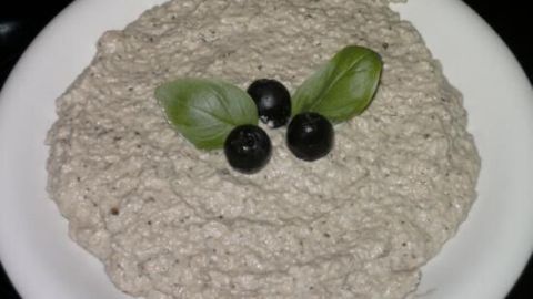 Ein cremiger Baba Ganoush ist auf einem weißen Teller angerichtet, garniert mit Oliven und frischen Blättern.