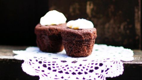 Zwei Schokomuffins mit flüssigem Kern stehen auf einer weißen Spitzenunterlage vor einem dunklen Hintergrund.