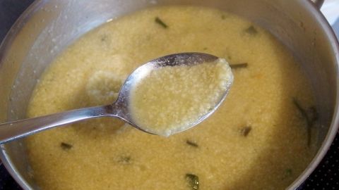 Eine Silberne Kelle rührt in einer tiefen Pfanne mit einer gelblichen Soße, die mit Butter-Chips gebunden ist.