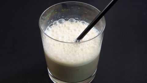 Colamilch ist ein ungewöhnliches, aber erfrischendes Getränk aus Cola und Milch, das durch Eiswürfel noch geselliger wird. Probiere diesen einzigartigen Mix aus der Kombination beider Zutaten aus dem Artikel aus! Ein Glas mit Colamilch und Eiswürfeln steht auf einem dunklen Tisch, während ein Strohhalm darin steckt und Blasen aufsteigen.