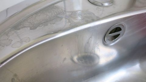 Neben der Spüle sind Seifenreste und Kalkflecken sichtbar, die auf einer glänzenden Edelstahloberfläche liegen.