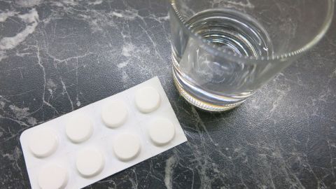 Mit einer Asprin-Tablette und ein wenig Wasser auf dem Pflaster heilt Herpes über Nacht viel schneller ab! Weiße Tabletten liegen auf einer Arbeitsfläche neben einem Glas Wasser, bereit zur Einnahme gegen Herpes.