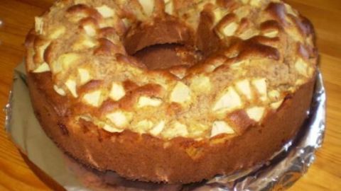 Ein saftiger Apfelrührkuchen liegt auf einer silbernen Unterlage und hat eine runde Form mit stückigen Äpfeln.