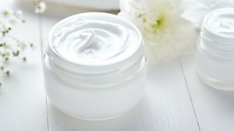 Eine weiße Salicylsäure-Creme steht auf einem hellen Tisch, umgeben von Blumen, und strahlt eine frische, saubere Atmosphäre aus.