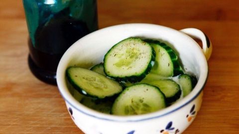 In einer Schüssel liegen frische Gurkenscheiben in einer Joghurt-Salat-Soße, daneben eine grüne Glasflasche.