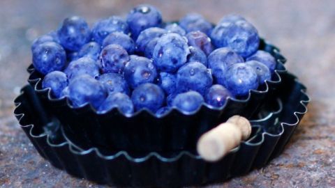 Eine schwarze Backform enthält frische, leuchtend blaue Blaubeeren, die auf einem rustikalen Tisch präsentiert werden.
