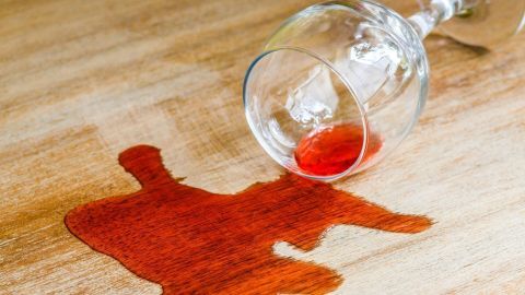 Rotweinflecken auf einem Fichtenholztisch mithilfe von Klößweiß (Pulver mit Zitrussäure) wegbekommen. Ein umgekipptes Weinglas liegt auf einem Holztisch, während Rotweinflecken sich auf der Oberfläche ausbreiten.