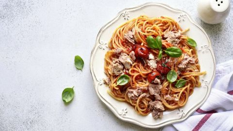 Spaghetti mit Tomaten-Thunfischsoße und frischem Basilikum auf einem eleganten Teller, umgeben von einer hellen Oberfläche.