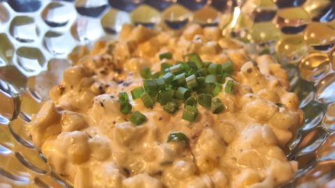 Ein cremiger Maissalat mit frischer Creme fraiche und gehacktem Schnittlauch ist in einer dekorativen Schale angerichtet.