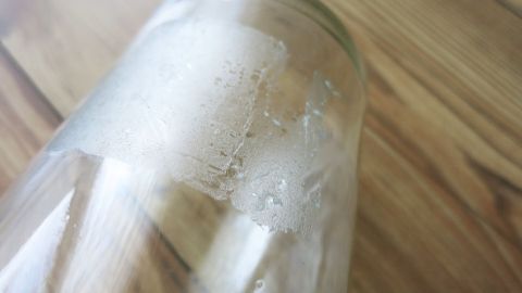 Ein Glas ist auf einer Holzoberfl&auml;che zu sehen, beschlagen mit Reinigungsmitteln, die zur Entfernung von Kleberesten verwendet werden.