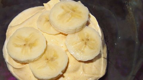Cremiger Bananenquark mit frischen Bananenscheiben in einer transparenten Schüssel, serviert auf einem Tisch.