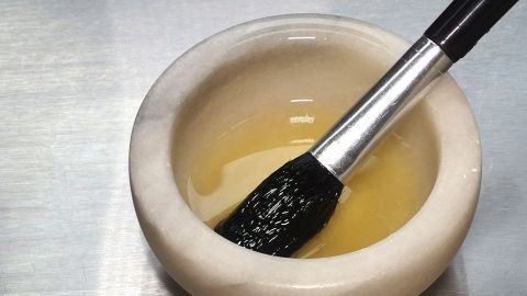 Eiweiß-Peeling: Eiweiß in eine Schale geben und leicht verrühren, dann mit den Händen oder Pinsel aufs Gesicht dünn auftragen. Ein Mörser enthält Eiweiß, während ein Pinsel darin eingetaucht ist, um die Anwendung für ein Peeling vorzubereiten.