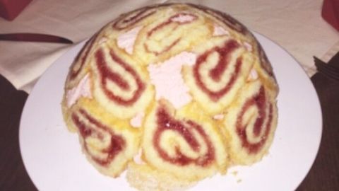 Eine runde Biskuit-Torte auf einem Teller zeigt eine Anordnung von Spiral-Rollen mit Himbeerfüllung, appetitlich dekoriert.