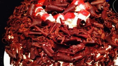 Eine üppige Schwarzwälder-Kirsch-Torte liegt auf einem Teller, dekoriert mit Schokoladenraspeln und Kirschen, bereit zum Genießen.