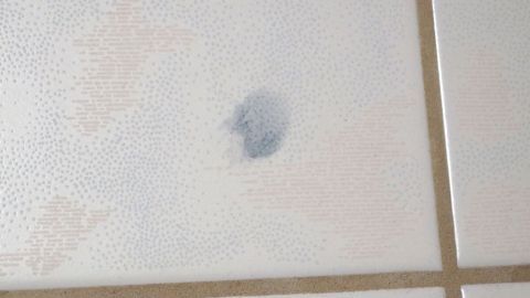 Ein blauer Farbfleck ist auf einer hellen Fliesenoberfläche sichtbar, was auf eine missratene Haarfarbe hindeutet.