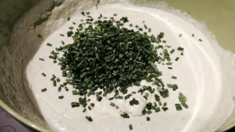 Ein cremiger Kräuter-Knoblauch-Dip wird in einer Schüssel mit frischen Kräutern zubereitet, umgeben von einer hellen Küchenumgebung.