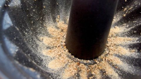 Nach dem Backen flutscht der Kuchen wie von selbst aus der Form.. Eine Kuchenform zeigt Krümel, die gleichmäßig um das zentrale Rohr verteilt sind, als Vorbereitung für das Backen.