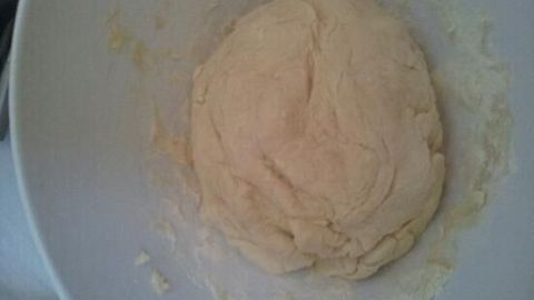 Der Pizzateig liegt in einer weißen Schüssel und wird gut durchgeknetet, ohne Hefe verwendet zu haben.