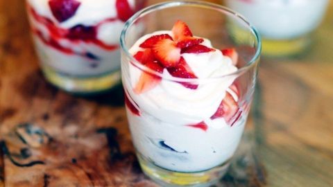 Gläser mit Beeren und Mascarponecreme stehen auf einem Holzbrett, umgeben von einer warmen, einladenden Küchenszene.