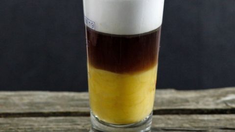 Ein Glas Espresso mit Eierlikör zeigt die Schichten der Getränke, während es auf einem rustikalen Holztisch steht.