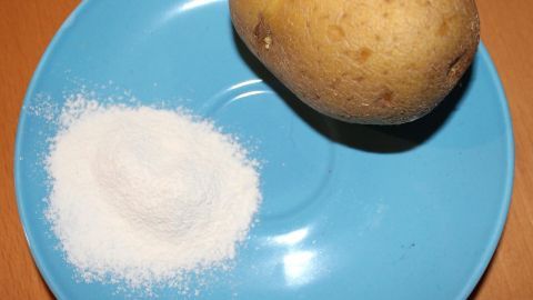 Das Kartoffelmehl brennt nicht und die Wunden heilen viel schneller. Eine Kartoffel liegt neben einer Portion Kartoffelmehl auf einem blauen Teller, bereit für die Anwendung auf wunder Haut.