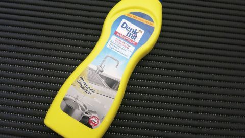 Gelbe Scheuermilch-Flasche liegt auf schwarzem Untergrund; Text auf Etikett: „Denk mit, Scheuermilch, mit frischem Zitrusduft.“