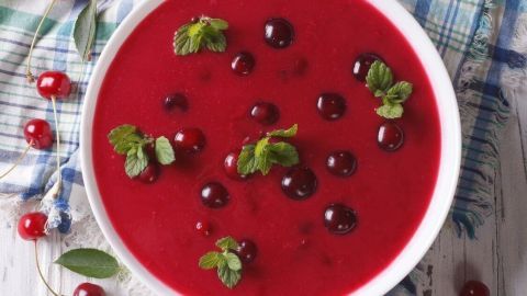 Eine glänzende Schüssel Kirschsuppe steht auf einem Holzuntergrund, umgeben von frischen Kirschen und blättrigem Dekor.