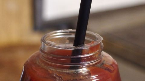 Schüttelorgien mit anschließender Spritzkatastrophe kann man sich mithilfe eines Strohhalmes ersparen. Ein Ketchupglas mit schwarzem Strohhalm steckt in der Flasche und steht auf einem Holzuntergrund in einer Küche.
