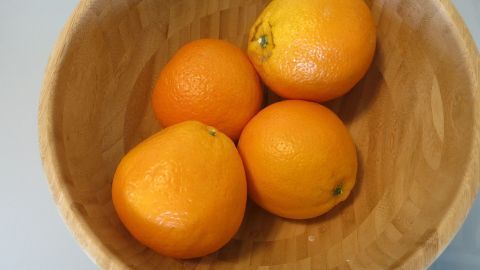 Vier frische Orangen liegen in einer Holzschüssel, bereit zur Pressung für frisch gepressten Orangensaft.