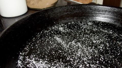 Pfannen, bei denen die Lebensmittel beim Garen (Braten) kleben bleiben, werden mit Salz gereinigt. Eine schwarze Pfanne liegt auf einem Herd, in der sich Salz befindet, das zur Reinigung der Pfanne verwendet wird.