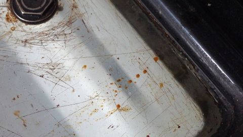 Mit heißem Wasser und einem Geschirrspültab eingebranntes Backofenfenster reinigen. Ein verschmutztes Backofenfenster zeigt eingebranntes Fett und Kratzer, was auf häufigen Gebrauch hinweist.