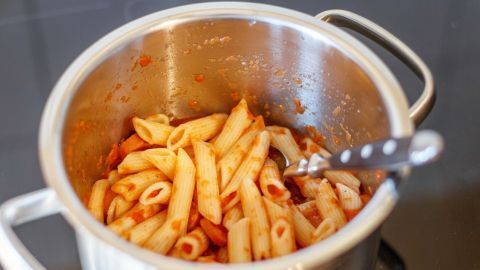 Penne-Pasta in einer silbernen Kochtopf, vermischt mit Tomatensauce, direkt auf einer modernen Kochfläche.