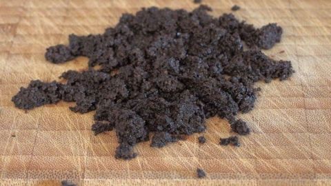 Schwarzer Kaffeesatz liegt auf einem Holzschneidebrett und absorbiert Gerüche wie Zwiebelgeruch in der Küche.