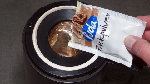 Effektives Reinigen von Thermoskannen mit kochendem Wasser und Backpulver. Eine Hand hält ein Päckchen Backpulver über eine offene Thermoskanne, bereit, es zur Reinigung hinzuzufügen.