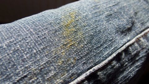 Eine Jeans mit Grasflecken liegt auf einem Tisch, während Klarspüler daneben bereitsteht, um die Flecken zu entfernen.