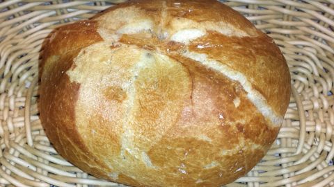 Ein knuspriges Aufbackbrötchen liegt in einem geflochtenen Korb und zeigt eine goldbraune, rustikale Oberfläche.