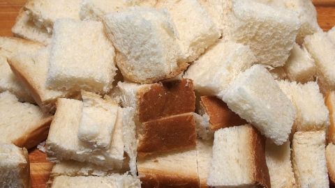 Würfelformige Brotreste liegen ungeordnet auf einem Holzbrett, bereit, um zu Paniermehl verarbeitet zu werden.
