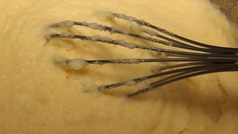 Kartoffelpüree wird mit einem Schneebesen glattgerührt, während es in einer Schüssel steht, um eine cremige Textur zu erzielen.