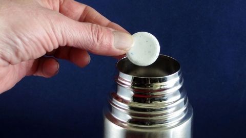 Eine Hand platziert eine Gebissreinigungstablette in eine Thermoskanne, um sie effektiv zu reinigen.