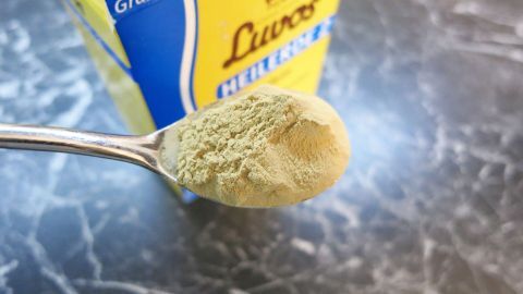 Ein Teelöffel Heilerde steht auf einem Tisch, umgeben von einer gelben Verpackung mit 480 Gramm.