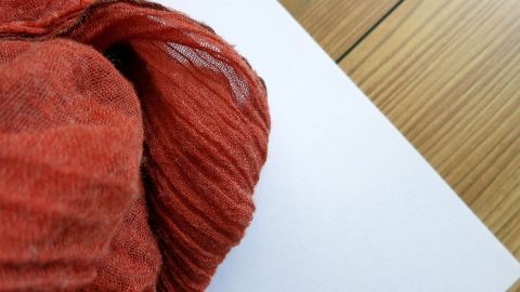 Wer sich unsicher ist, ob ein Stoff abfärbt, kann dies vor dem Waschen ganz leicht testen: Eine Ecke von dem besagten Stoff anfeuchten, auf einem weißen Papier reiben und schauen, ob Farbflecken auf dem Papier sichtbar sind. Ein leuchtend orangefarbener Stoff liegt auf einem weißen Blatt Papier, während der Hintergrund aus hellem Holz besteht.