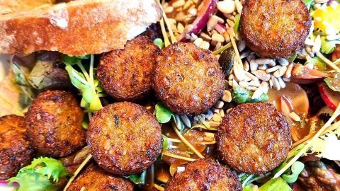 Kleine, frittierte vegetarische Bulettchen liegen auf einem bunten Salat mit Brotstücken im Hintergrund.