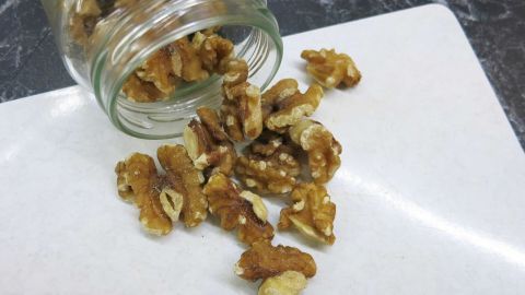 Walnüsse fallen aus einem Glas auf eine helle Oberfläche, was das Schälen erleichtert und für Rezepte bereitstellt.