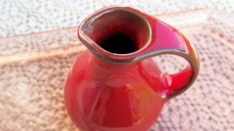 Eine rote Vase mit einem kleinen Riss steht auf einem hellen Untergrund und zeigt Anzeichen von möglicher Reparatur.