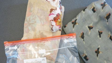 Seidentücher liegen zusammen auf einem Tisch, während eines in einer durchsichtigen Tüte verstaut ist.