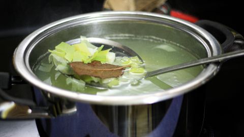 Ein Topf mit Gemüsefond köchelt auf dem Herd, während frische Zutaten wie Lauch und Lorbeerblätter im Wasser schwimmen.