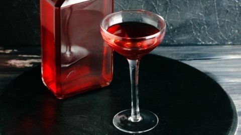 Eine geschmackvolle Flasche Tee-Likör steht neben einem eleganten Glas, das mit dem leuchtend roten Getränk gefüllt ist.
